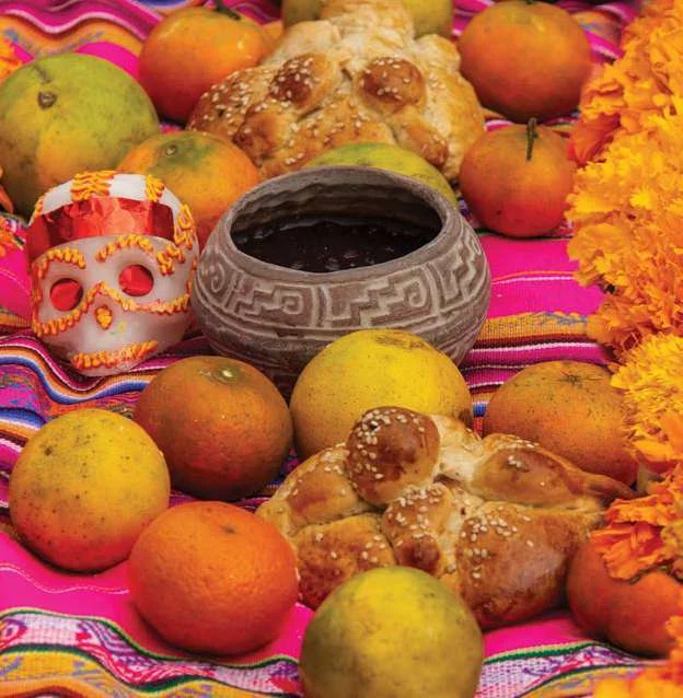 Pan de muerto, frutas y una taza de barro en una ofrenda